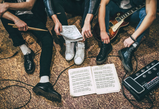 Music band repetition Repetition of rock music band. Cropped image of guitar players and drummer are sitting on the floor at rehearsal base with notes. Top view