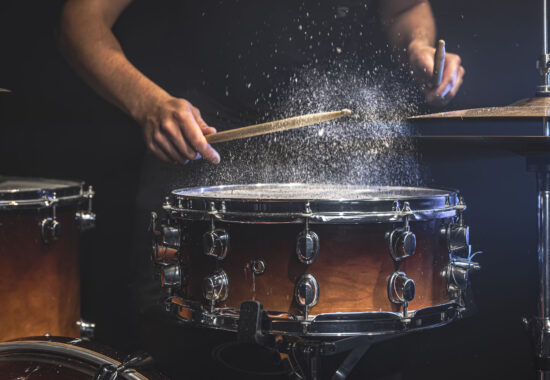 The drummer plays the snare drum with splashing water. A male drummer plays snare drum with drumsticks in a dark room.